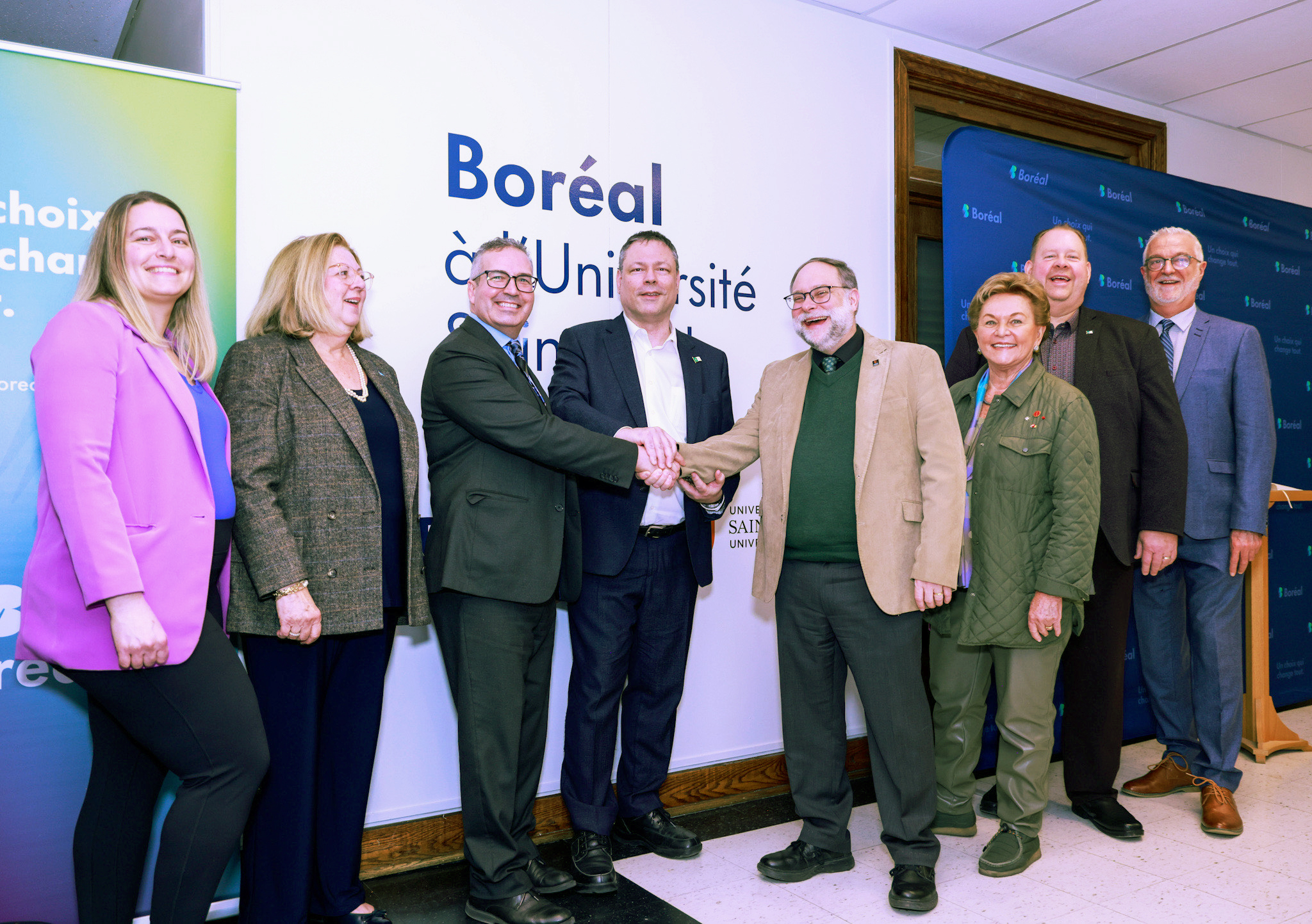 A group of people stands together in front of a large banner, smiling and engaging with each other.